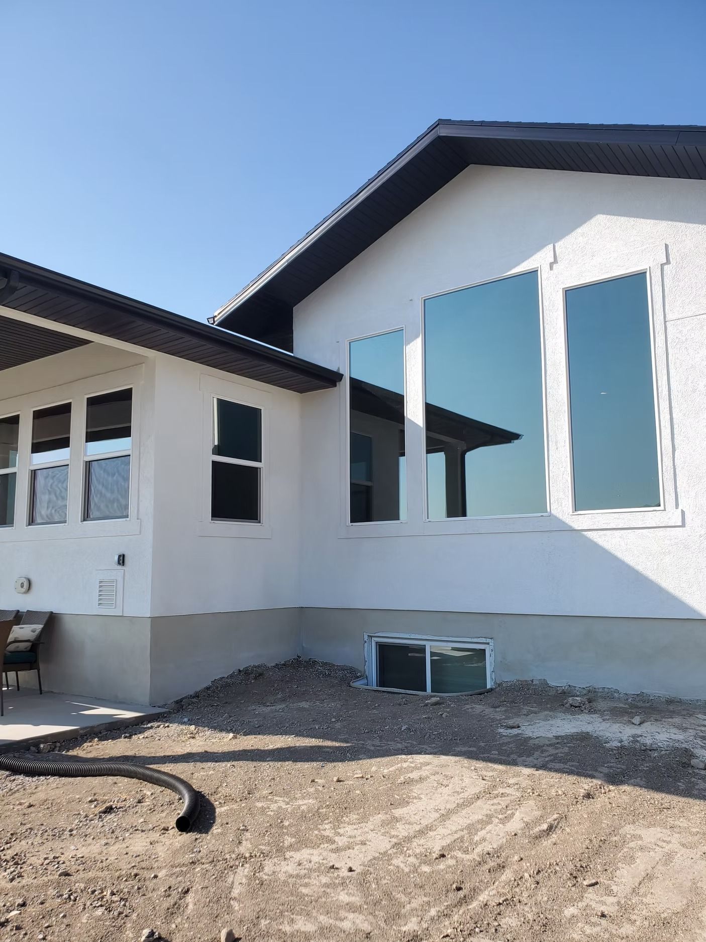 Exterior of a white stucco house with several windows, gravel, and a blue sky.
