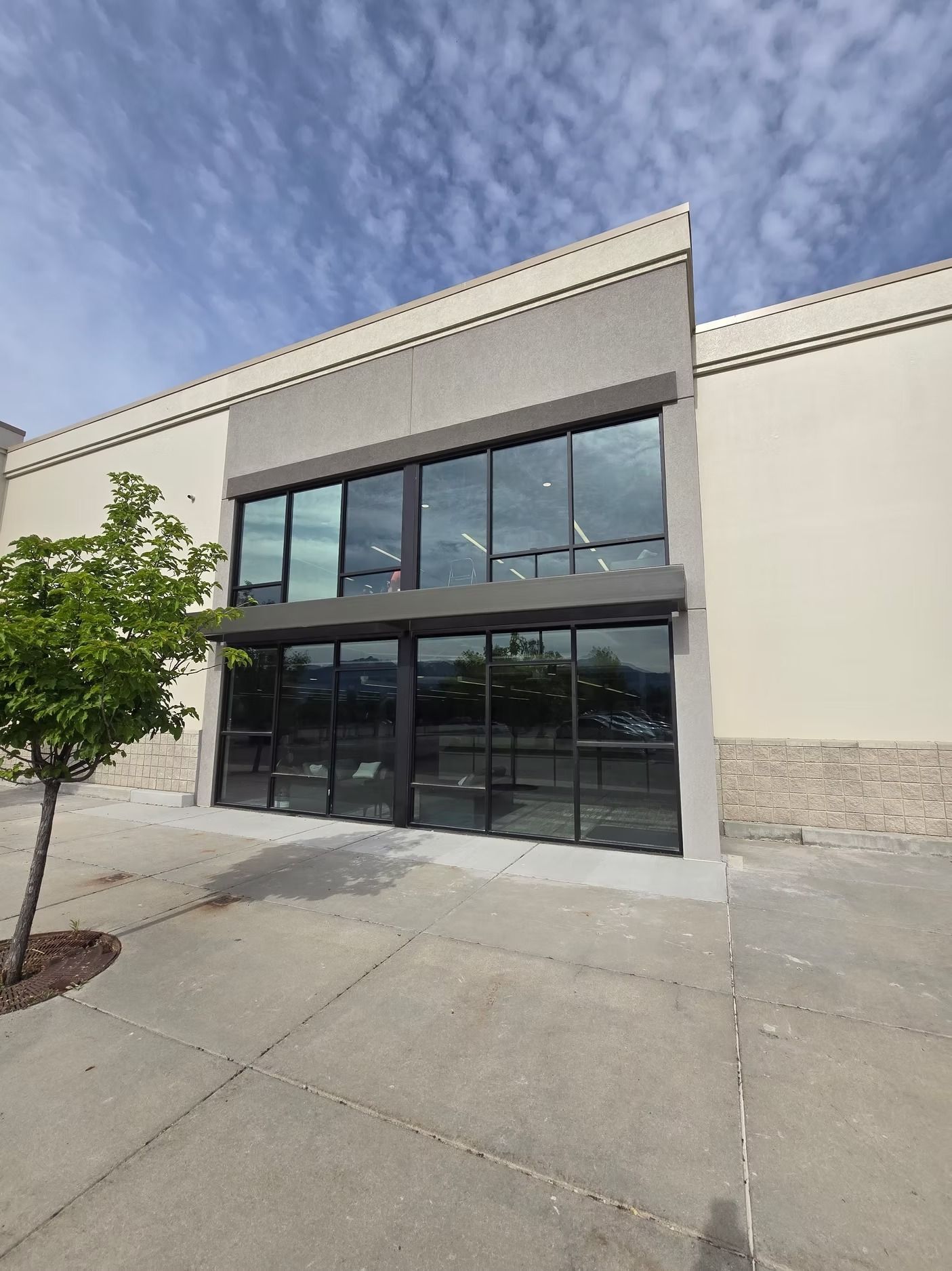 Exterior of a commercial building with large glass windows and gray accents under a cloudy sky.
