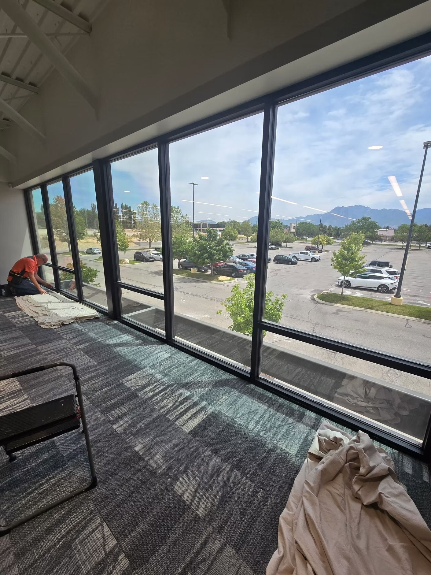 Large windows looking out at a parking lot. A person works inside on floor near the windows.