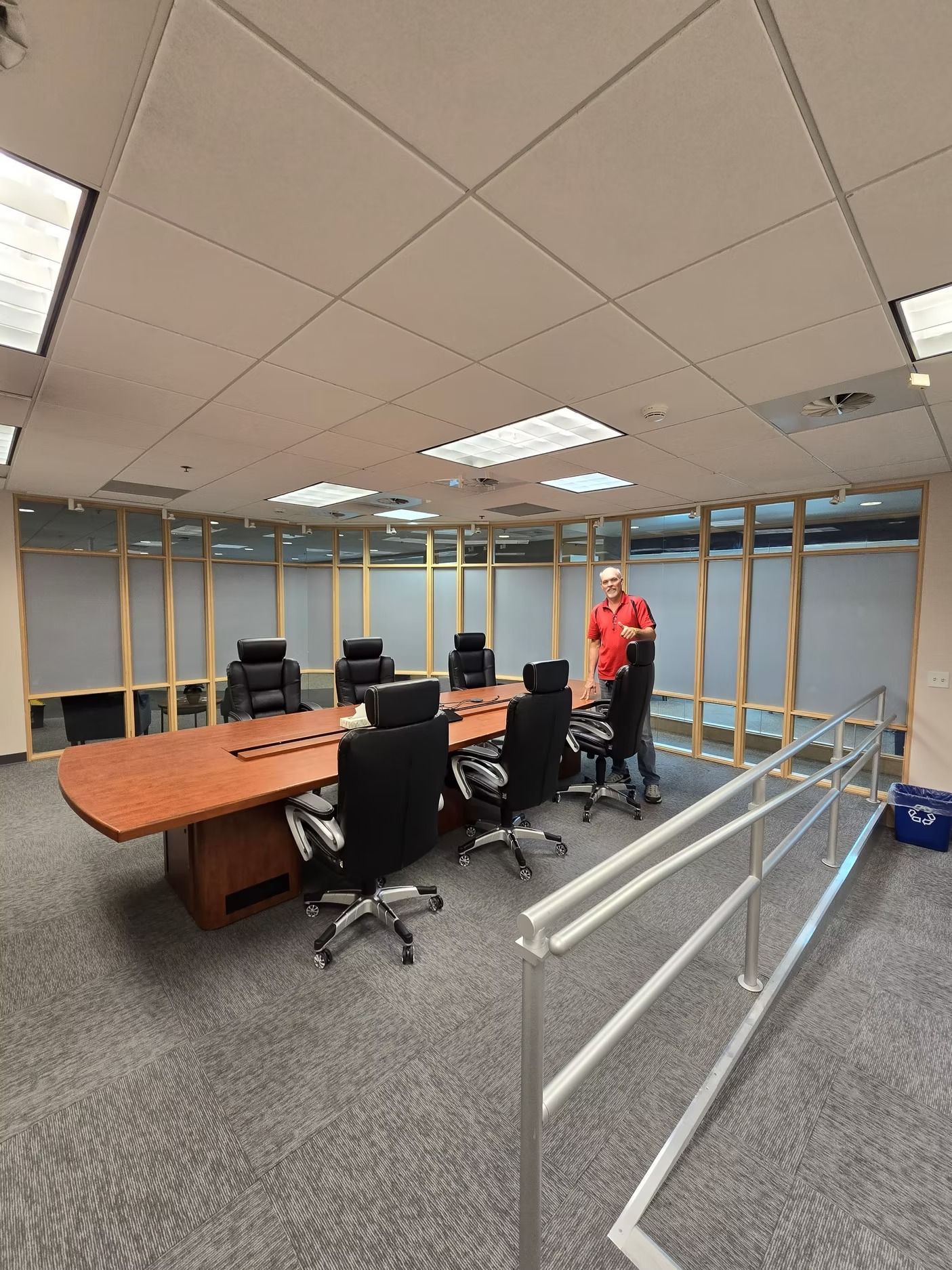 Conference room with a large table, black chairs, and a person standing near a metal ramp.