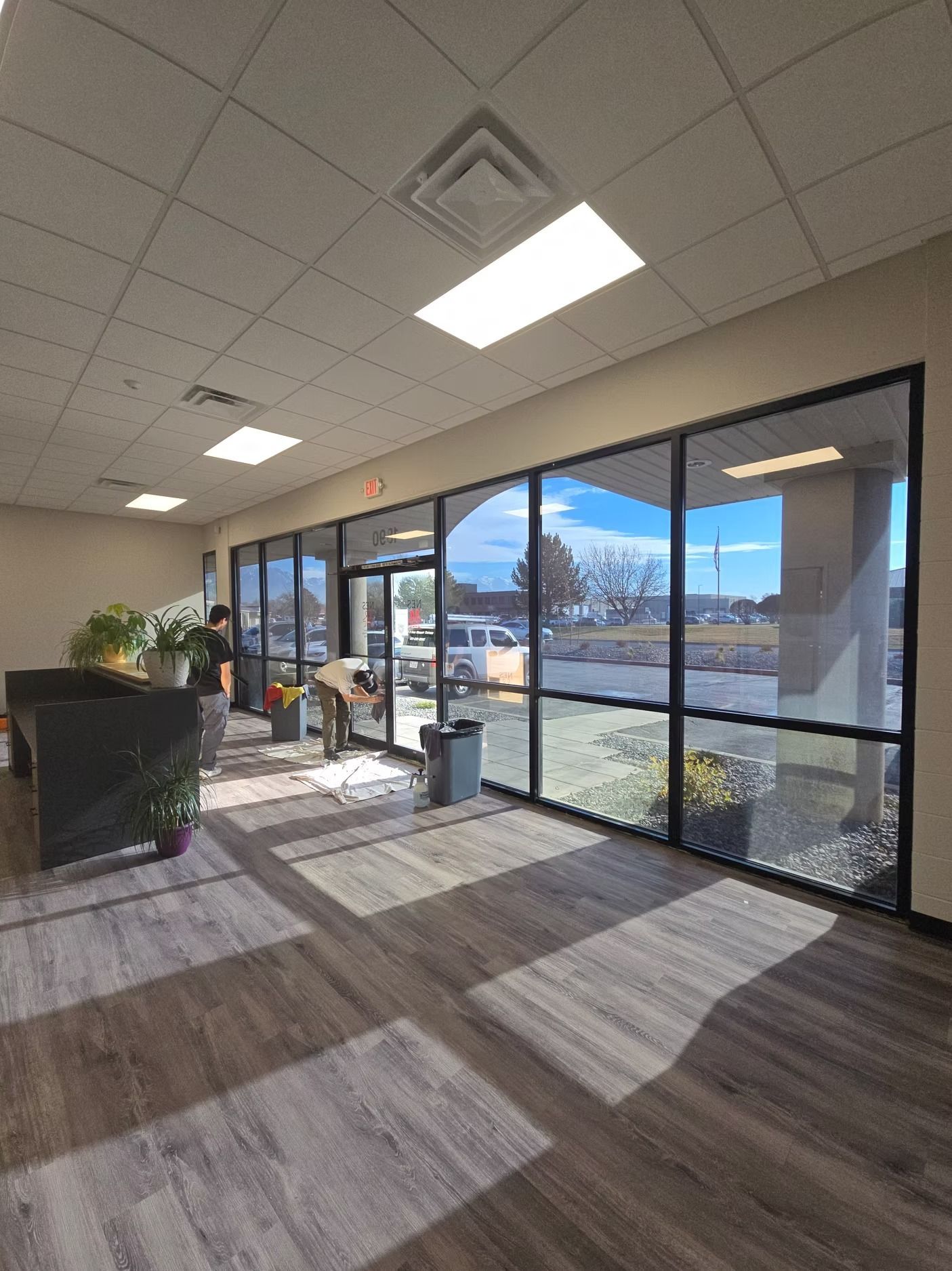 Interior shot with large windows, sunlight, and two people working near the entrance.