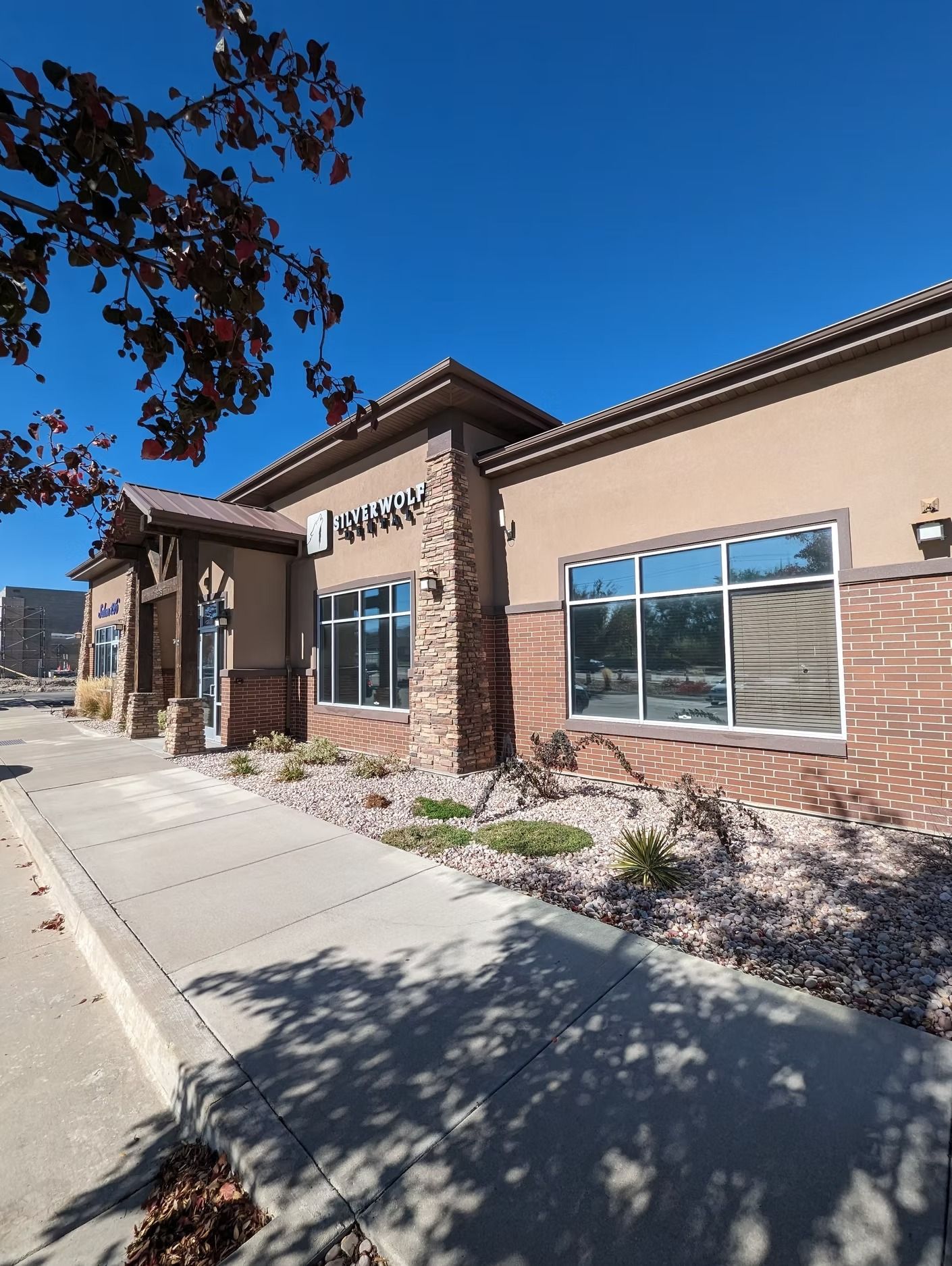 A tan and brick building with large windows and a sign against a bright blue sky.