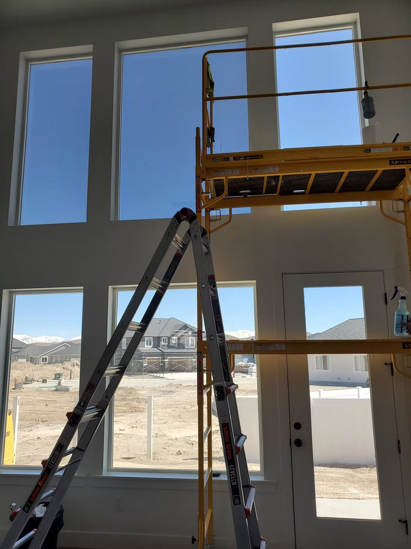 Interior with tall windows, ladder, and scaffolding; construction site visible outside.