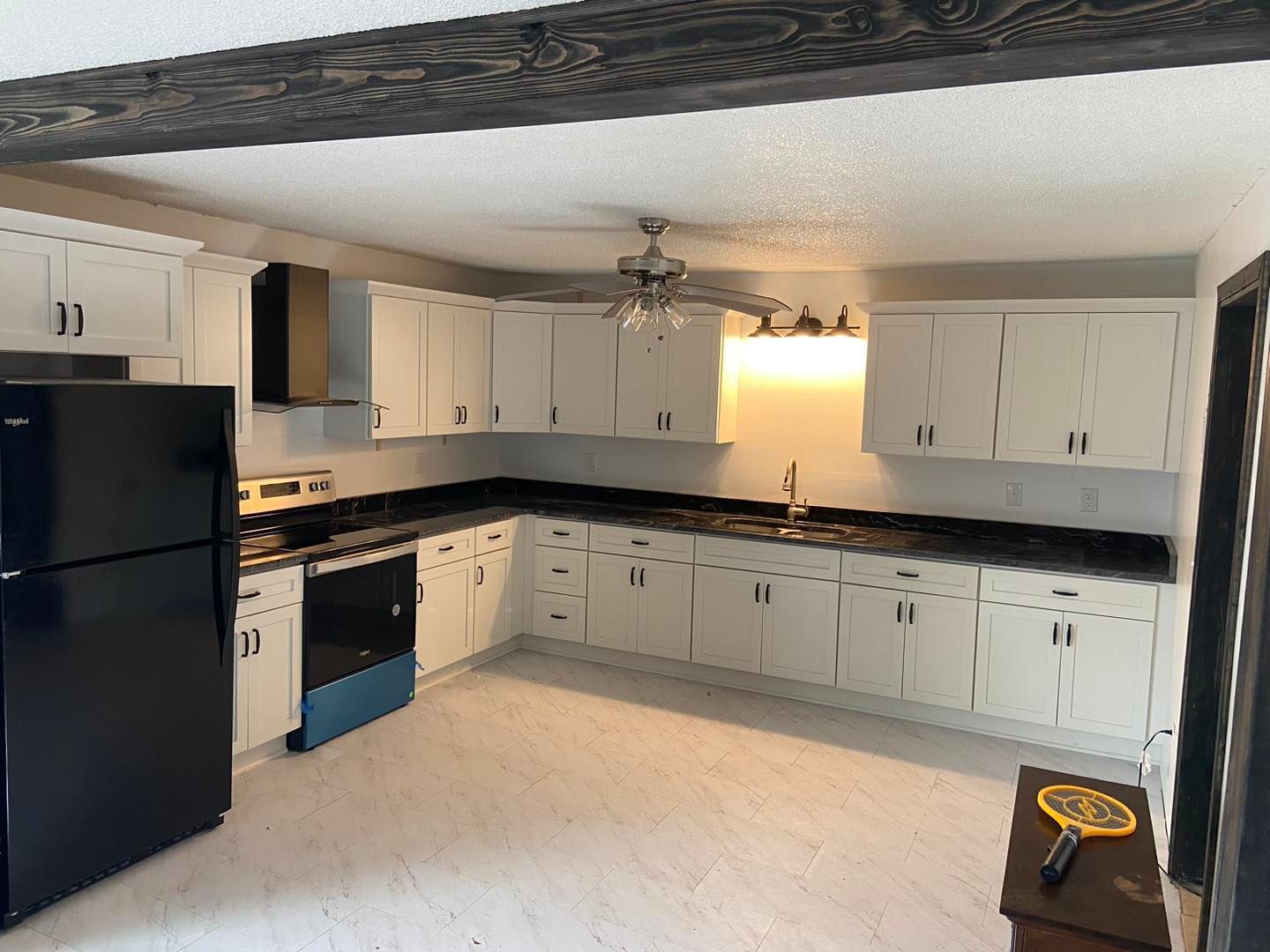White kitchen with black appliances, countertops, and dark wooden beam.