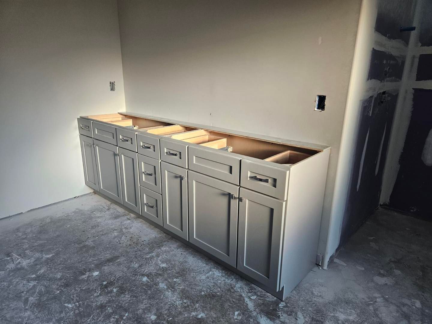 Bathroom vanity cabinet, grey, installed against wall, unfinished construction.