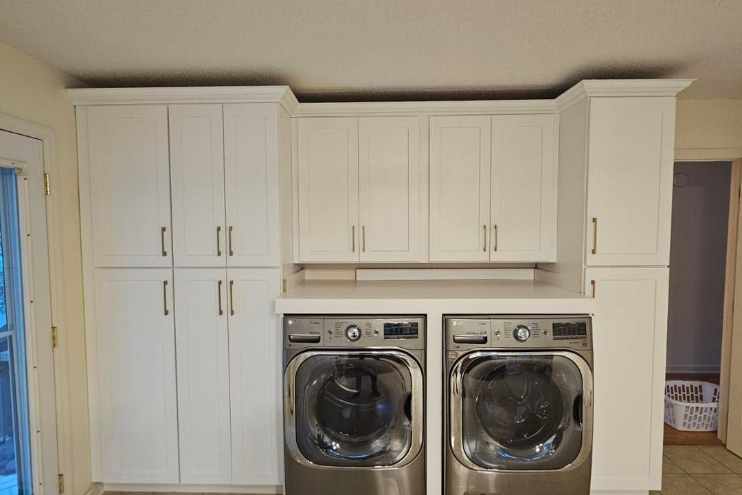 White laundry room with washer and dryer, cabinets above.