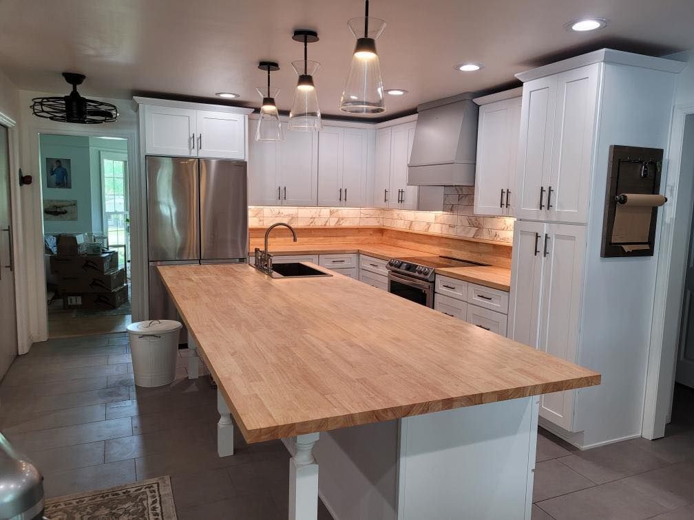 Spacious white kitchen with light wood countertops and a large island. Stainless steel appliances.