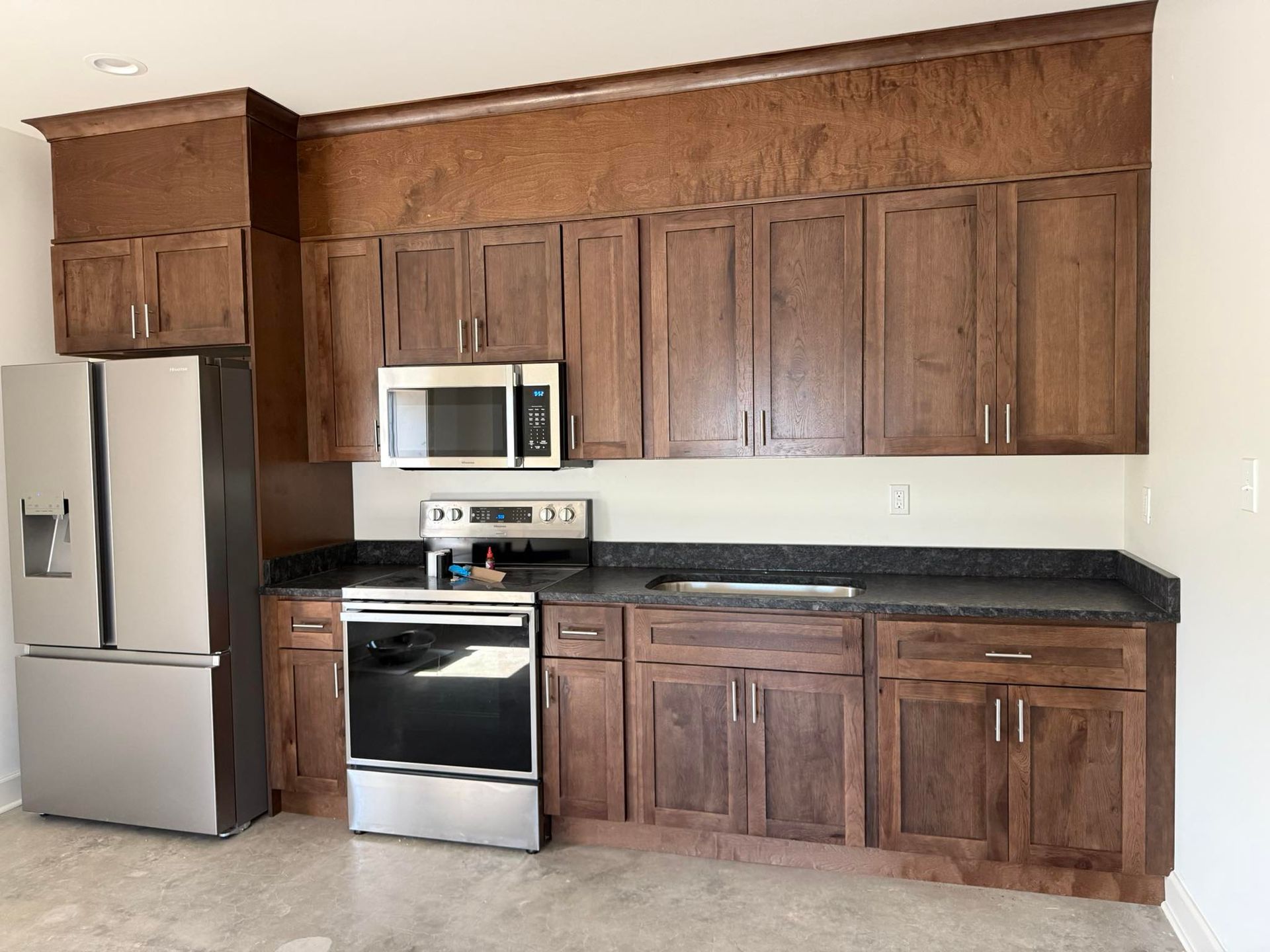 Brown kitchen cabinets and appliances in a modern space. Black countertops and a stainless steel refrigerator.