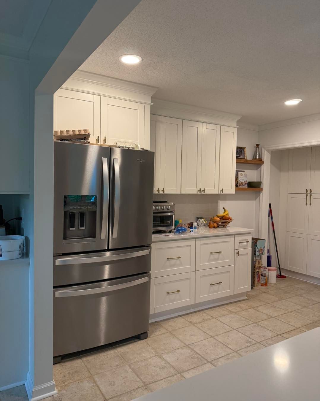 White kitchen with stainless steel refrigerator, white cabinets, and tile floor.