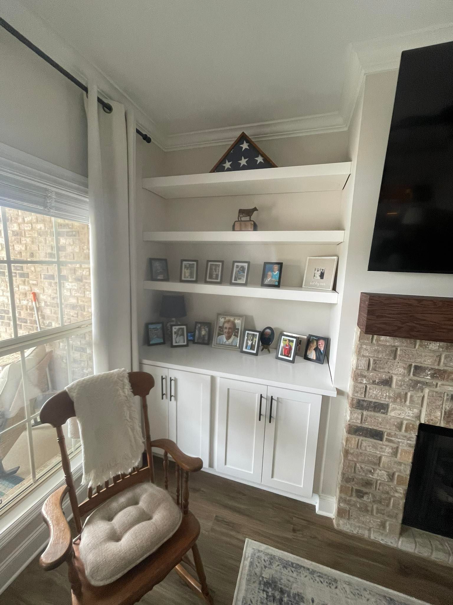 Built-in white bookshelves with framed photos and a folded American flag. A rocking chair sits nearby.