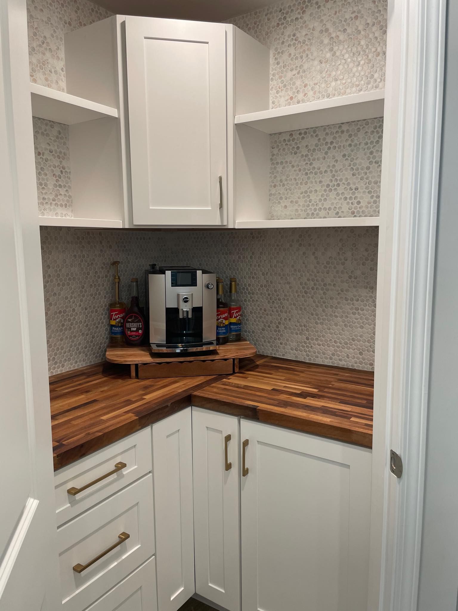 Built-in coffee station with white cabinets, wood countertop, coffee machine, and tile backsplash.