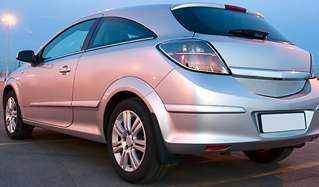 Un coche hatchback plateado aparcado al aire libre bajo un cielo oscuro.