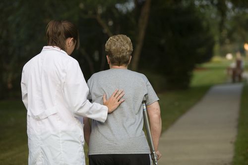 a nurse is helping a woman with crutches walk down a sidewalk .