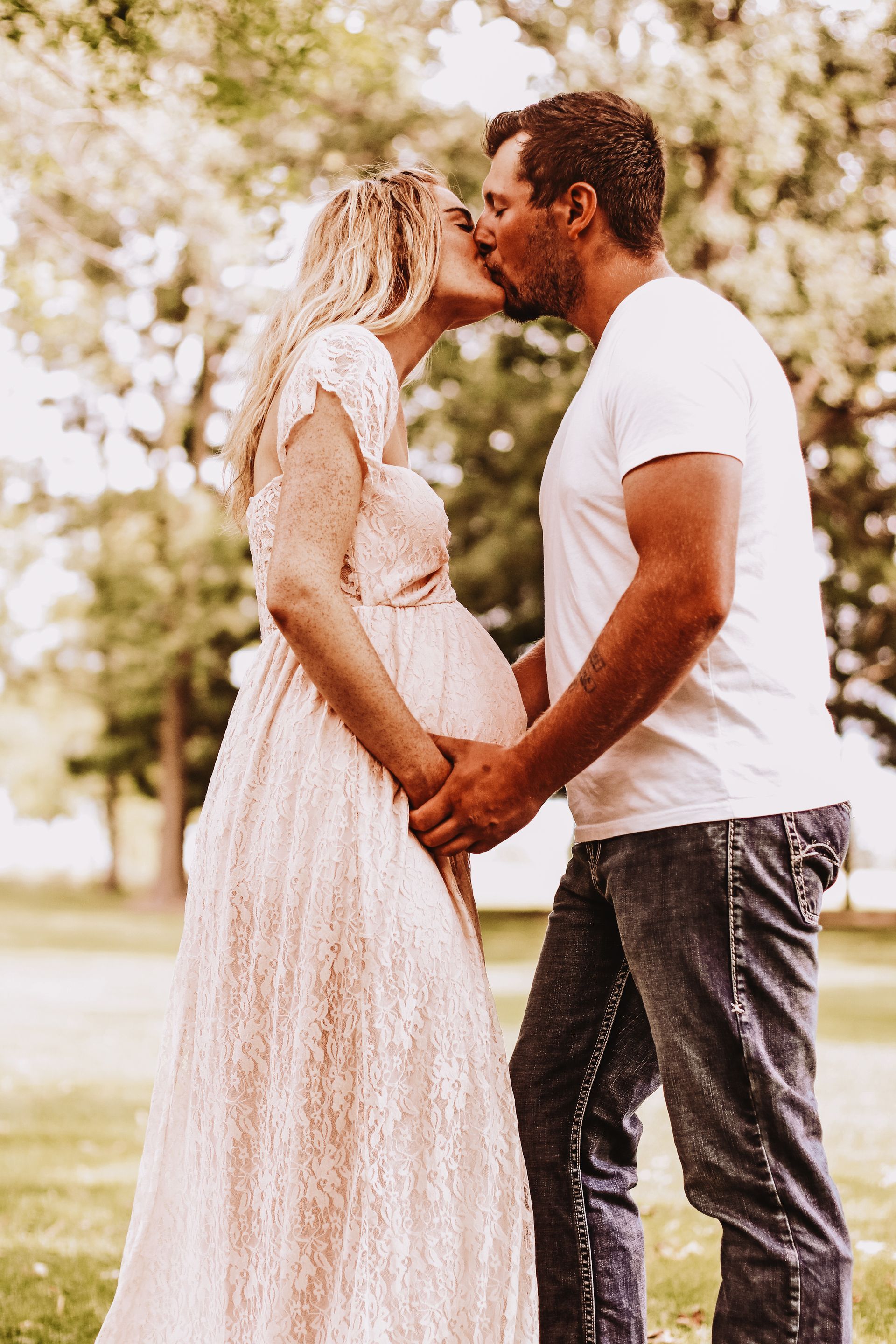 A pregnant woman is standing in a field of sunflowers with her husband and daughter.