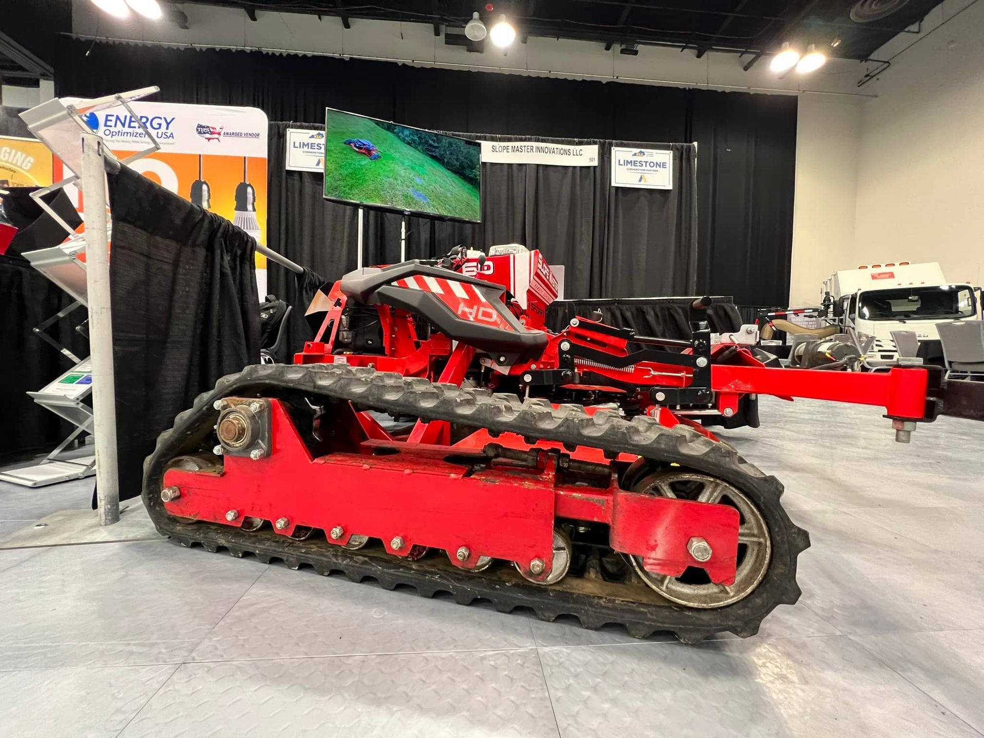Red tracked vehicle at a trade show, with a screen and black backdrop.