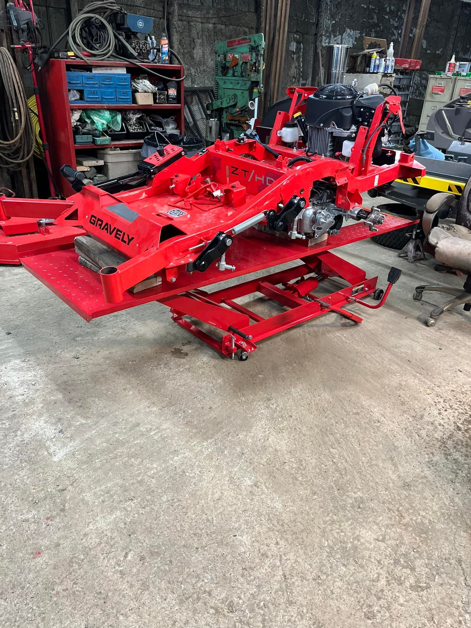 Red motorcycle lift supporting a motorcycle frame in a cluttered workshop.