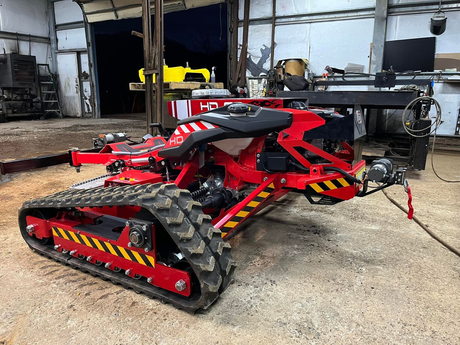 Red tracked robot with black and yellow hazard stripes, inside a workshop.