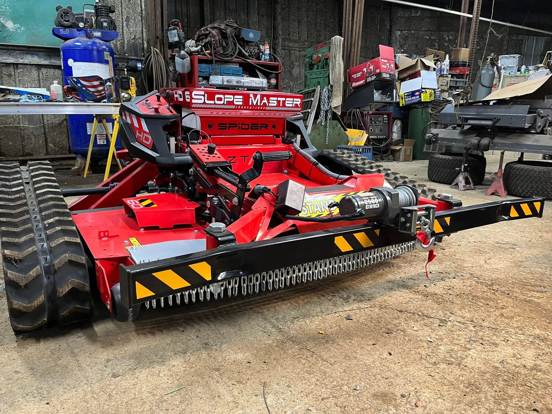 Red and black tracked brush cutter in a workshop.