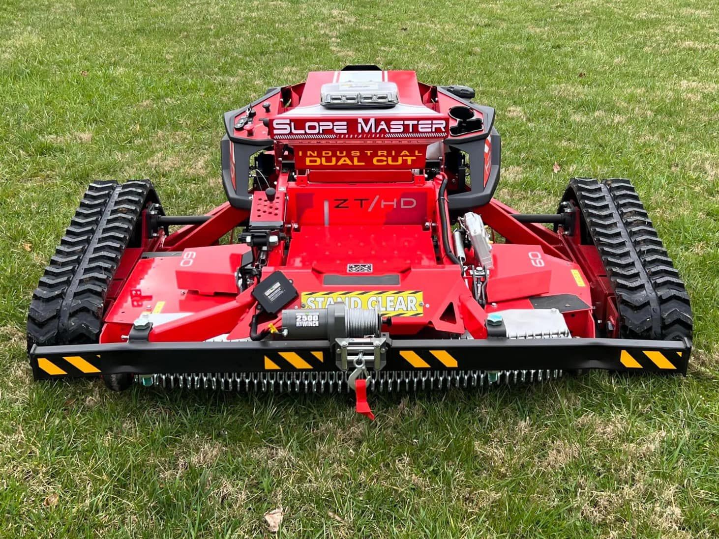 Red Slope Master mower on green grass with black tracks.