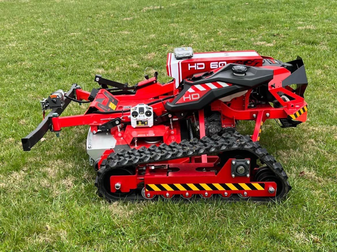 Red and black remote-controlled robot mower on green grass with treads.