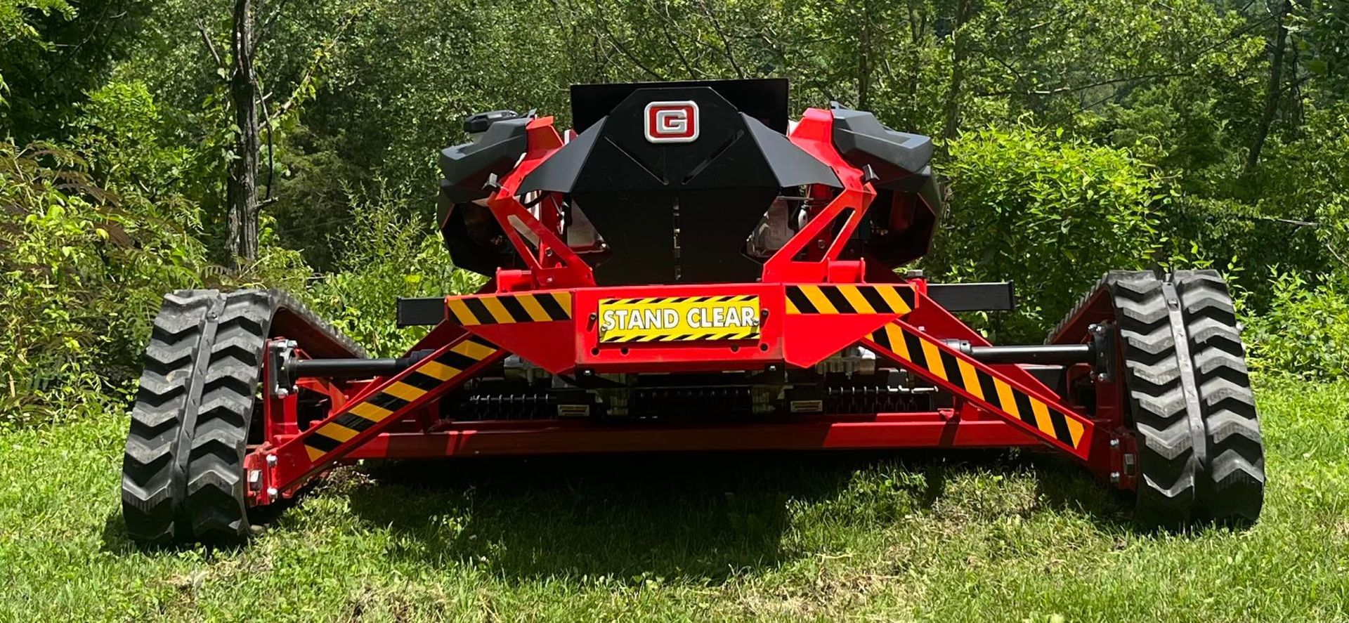 Red and black heavy machinery on a grassy field with thick tires and black and yellow striped bars.