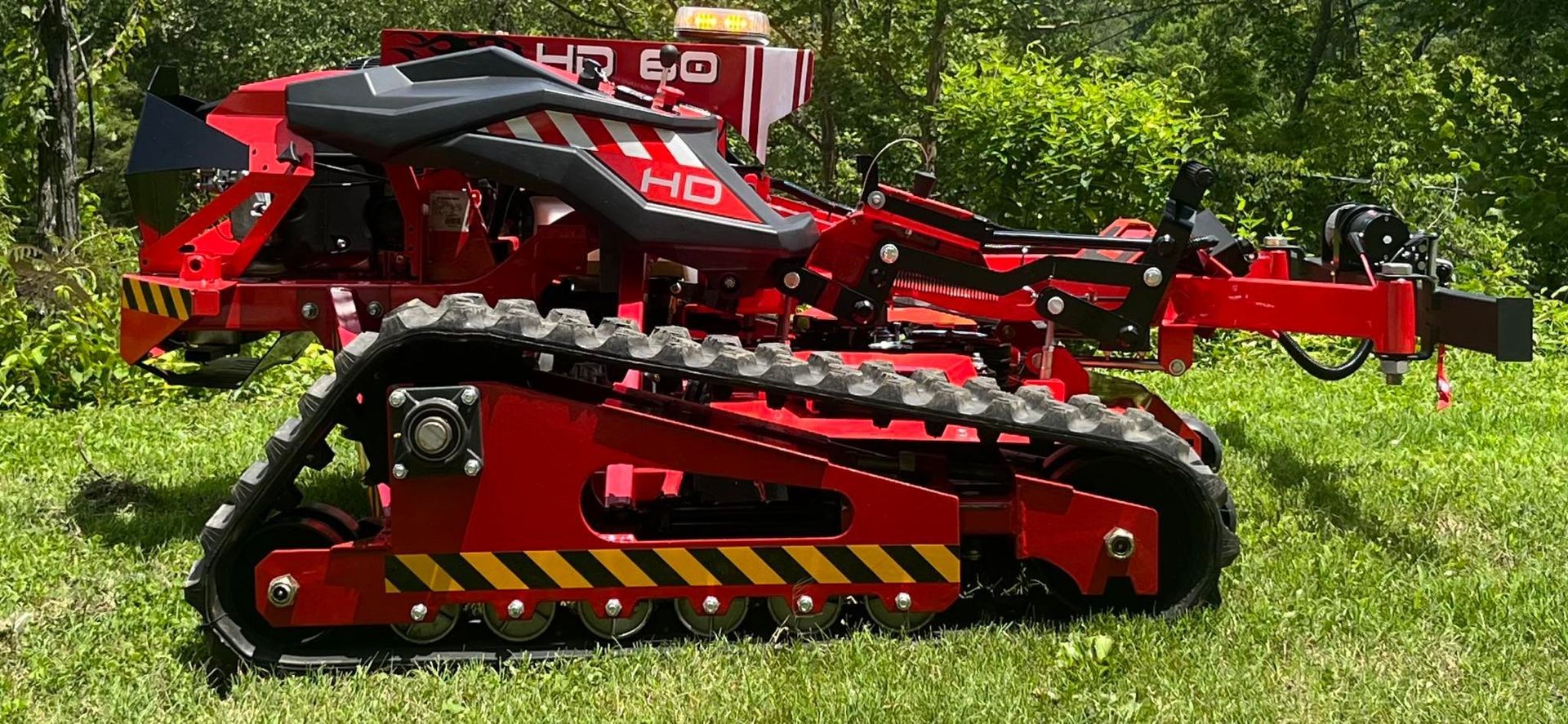 Red and black heavy-duty brush cutter with tracks on grassy ground.