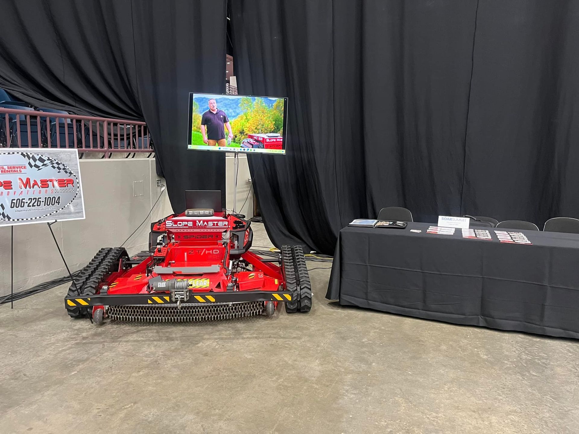 Red and black tracked robot with a TV screen in a convention hall setting.