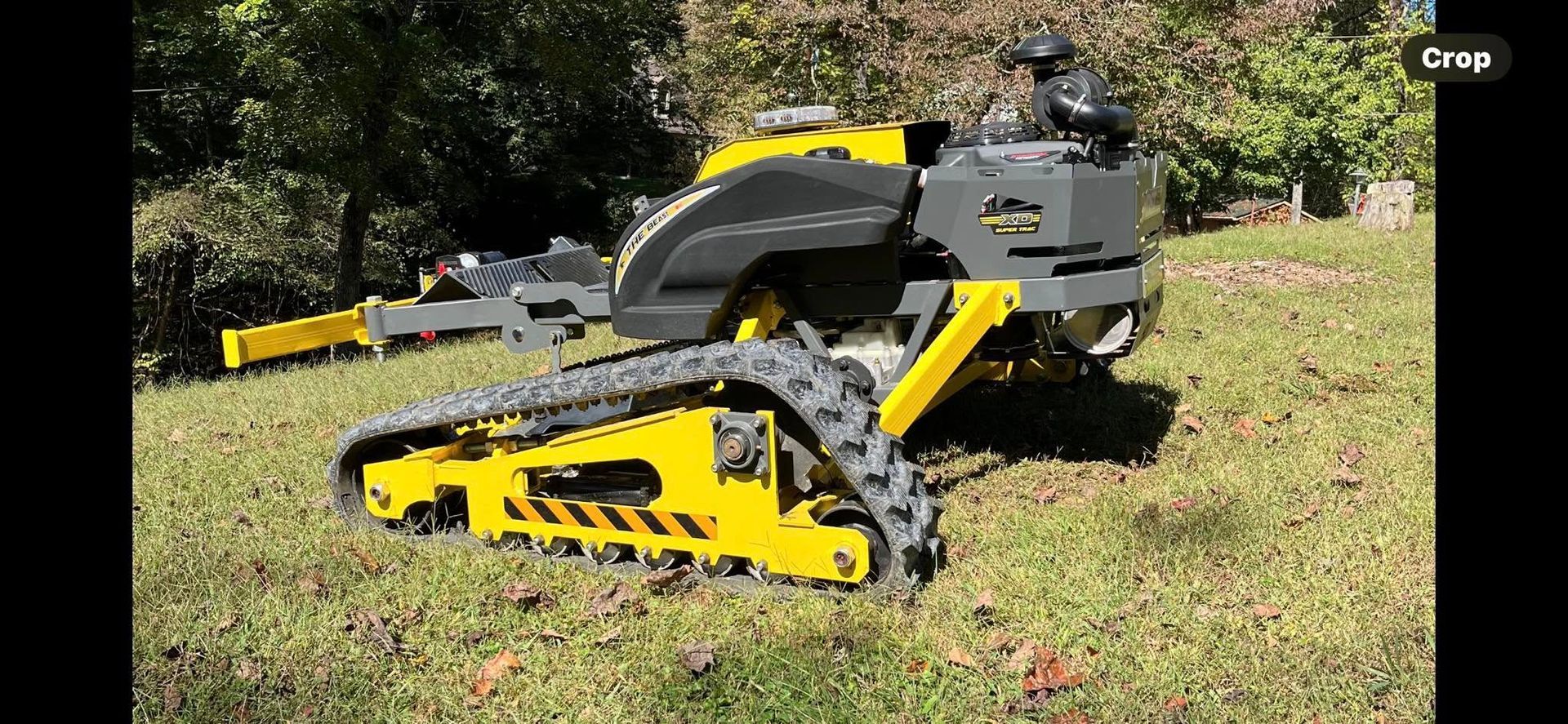 Yellow and black tracked robot on grass in front of trees.