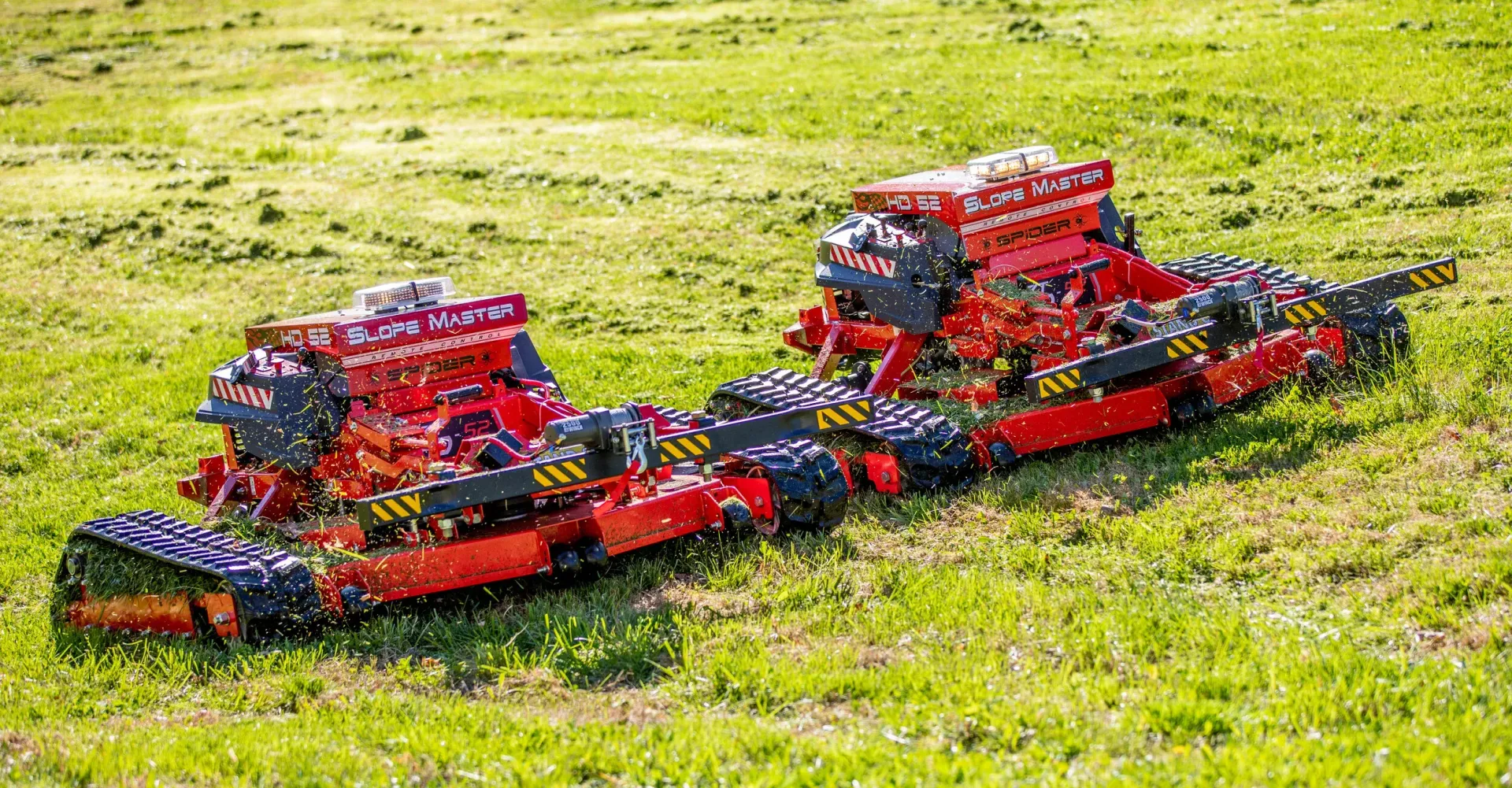 Two red and black Lego-like machines on a grassy field, possibly for agricultural use.