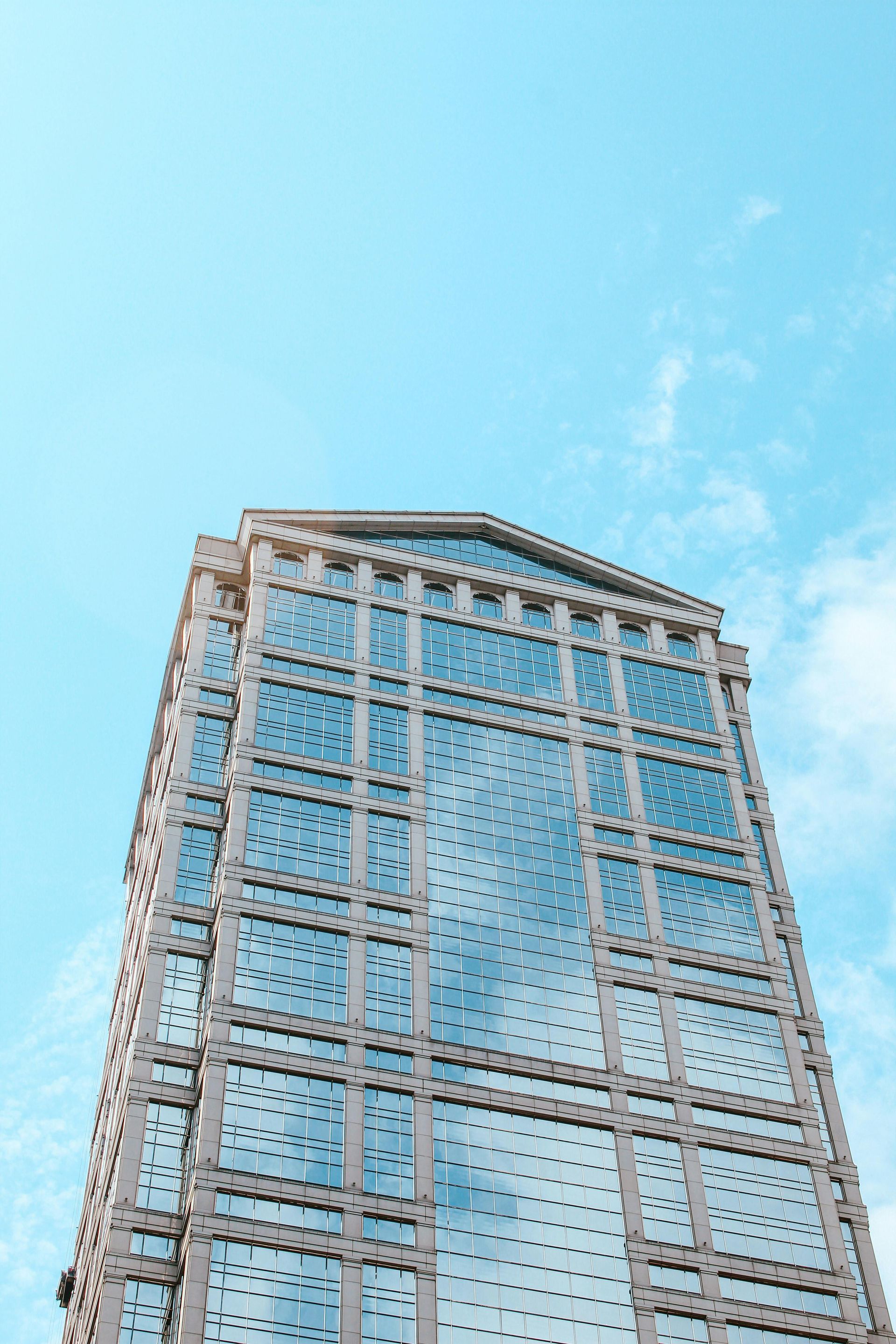 Tall glass skyscraper against a bright blue sky with scattered white clouds.