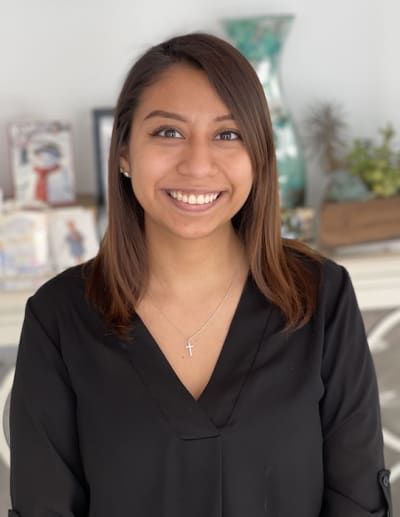 A woman wearing a black shirt and a cross necklace is smiling for the camera.