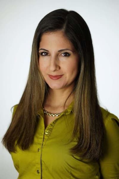 A woman with long hair is wearing a green shirt and a necklace.