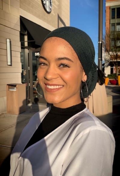 A woman wearing a turban is smiling in front of a building