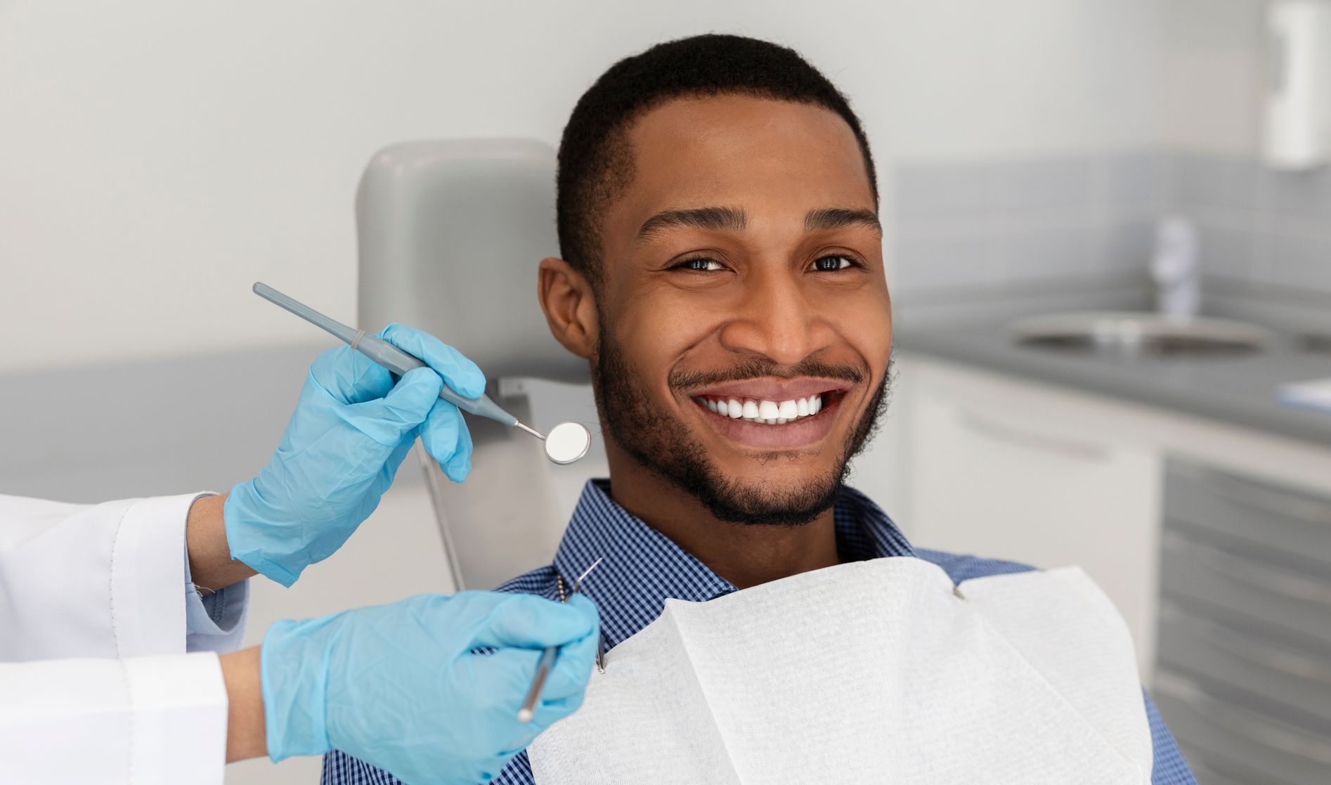 A man is sitting in a dental chair while a dentist examines his teeth.