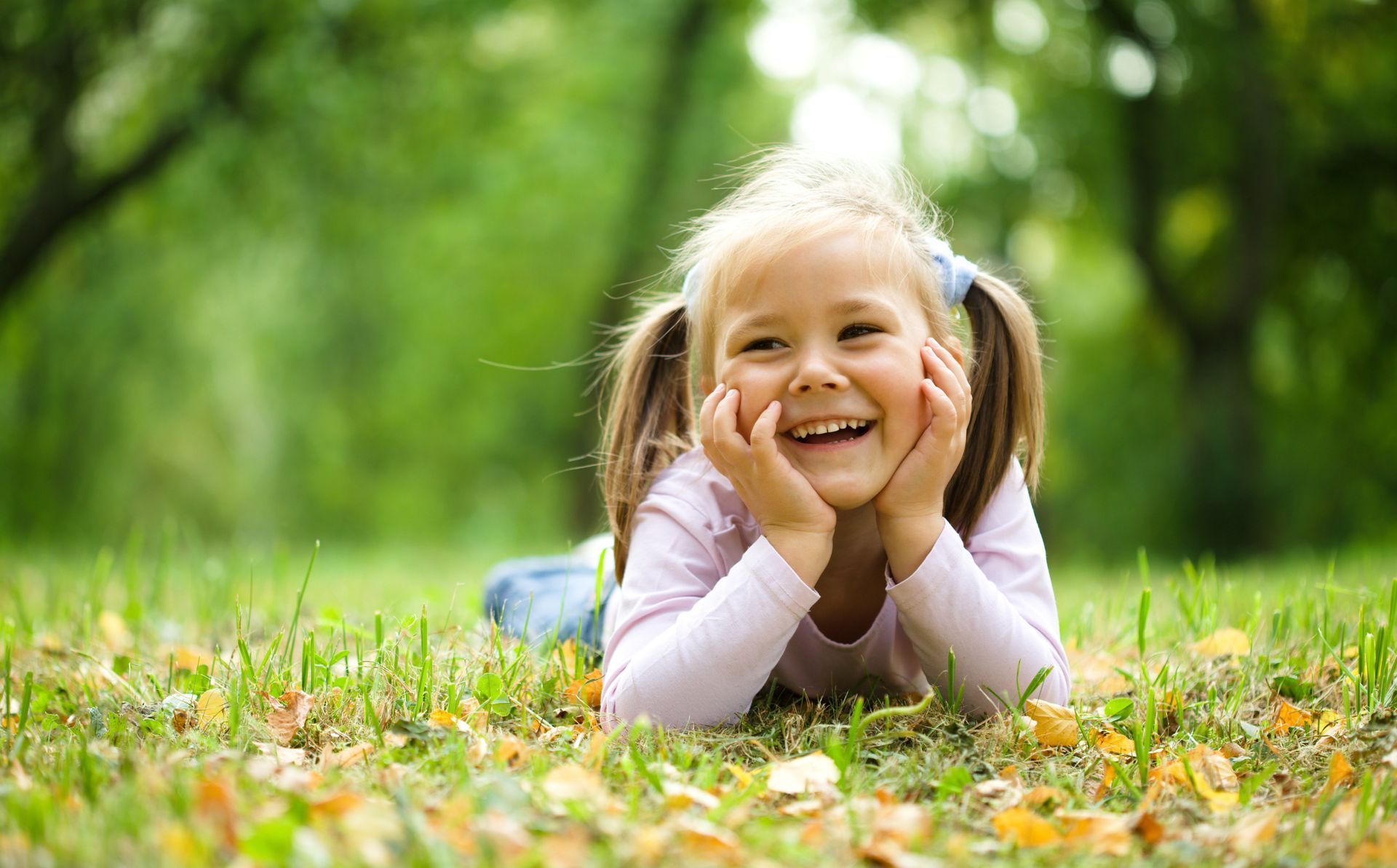 A little girl is laying on her stomach in the grass and smiling.