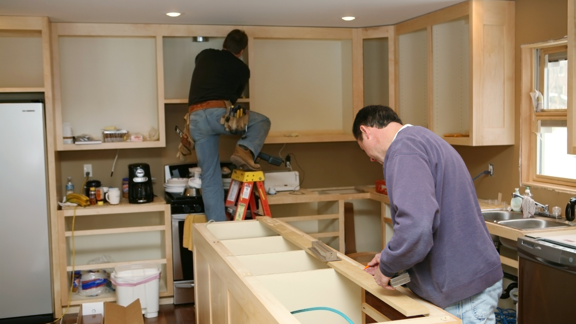 Two people installing kitchen cabinets. One on a step stool, one working at island.