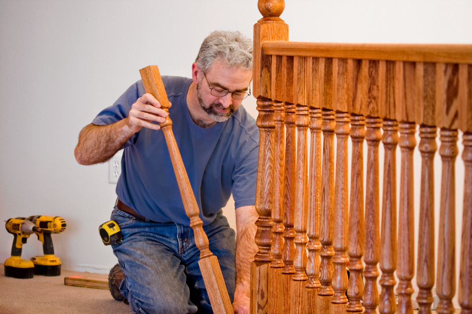 Man installing wooden stair railing, kneeling, in a house.