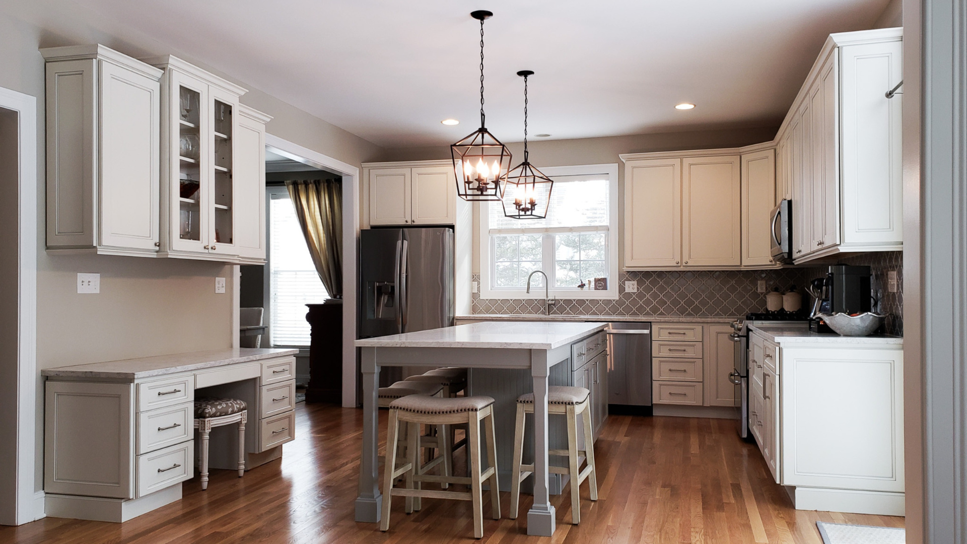 Cream-colored kitchen with wooden floors and a central island, featuring cabinets, a refrigerator, and pendant lights.