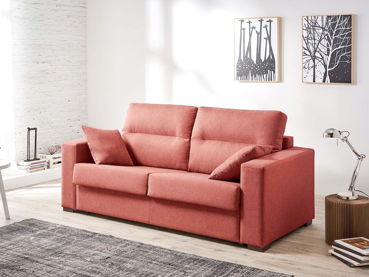 un sofá rojo está sentado en una sala de estar con dos cuadros en la pared .