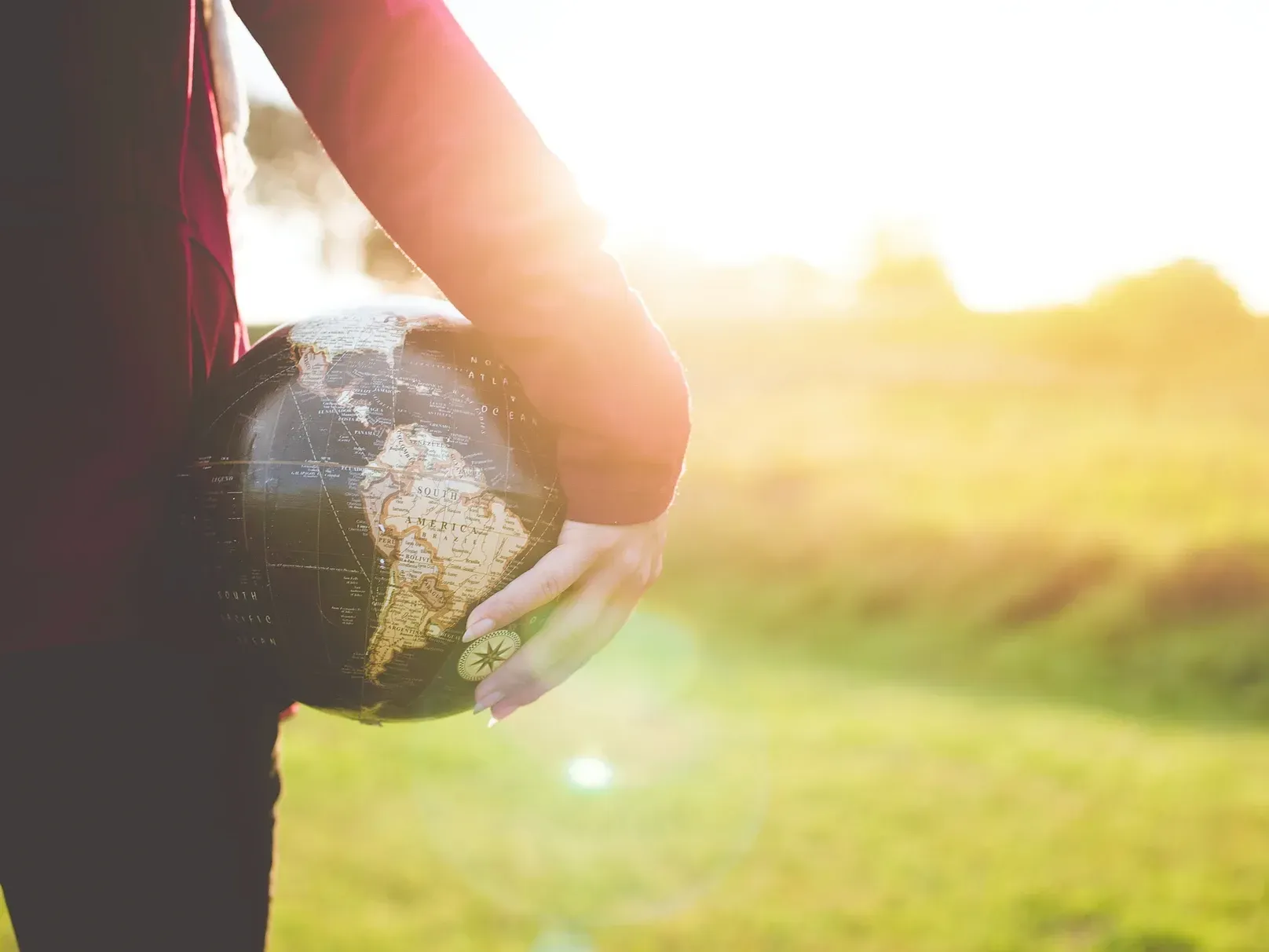 A person is holding a globe in their hands in a field.