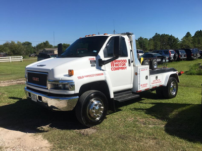White GMC tow truck with company logo parked on grass, sunny day.