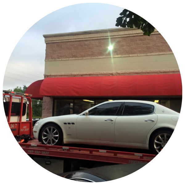 White Maserati sedan on a tow truck in front of a brick building with a red awning.