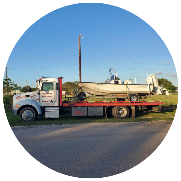 Tow truck with a white boat on its flatbed, parked on a road. Blue sky in the background.