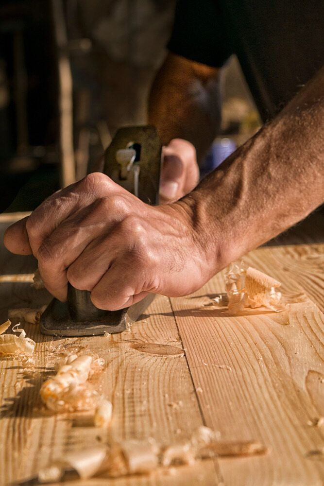 A Man Is Using A Plane To Plane A Piece Of Wood — CBY Carpentry & Renovations In Dubbo, NSW
