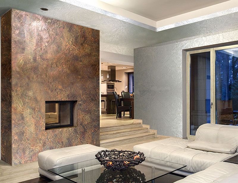 Soggiorno con camino color rame, divano in pelle bianca, tavolo in vetro e vista sulla cucina.