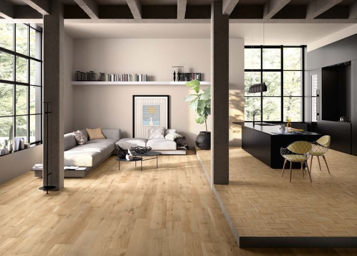 Soggiorno moderno con pavimenti in legno chiaro, divano grigio e ampie finestre.