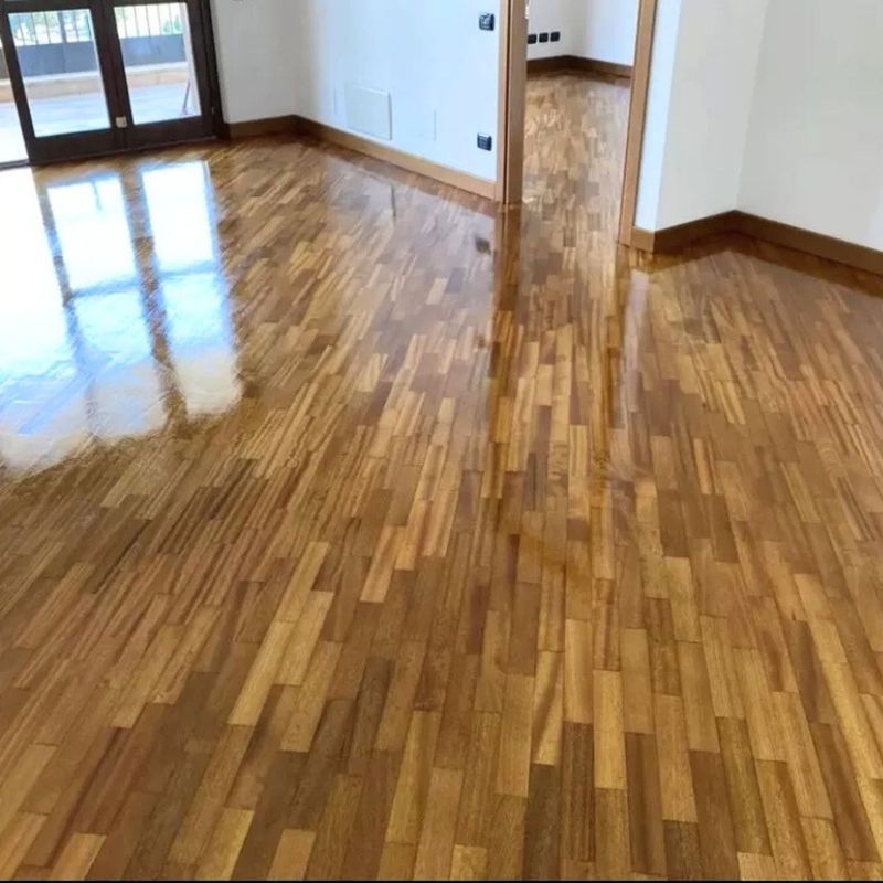 Pavimento in legno marrone chiaro e lucido in una stanza vuota, con riflessi luminosi e porte.