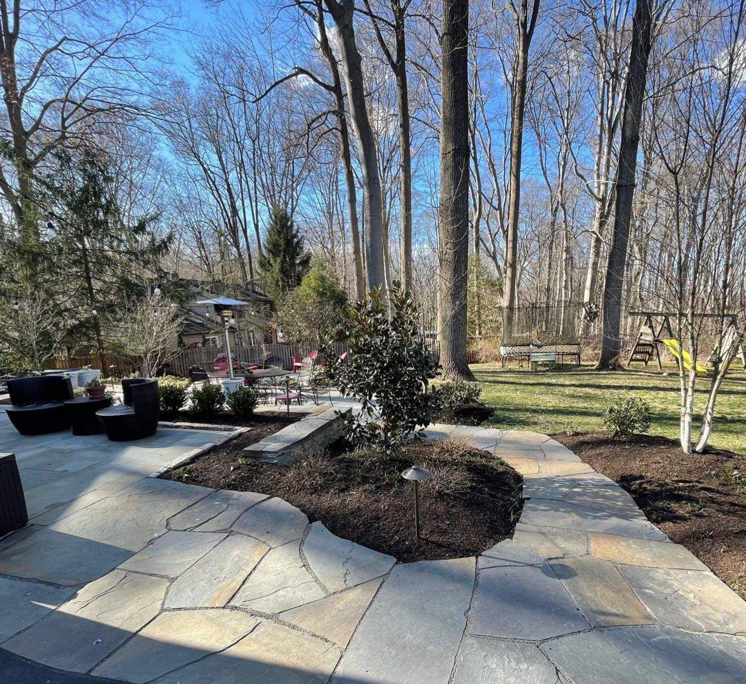 A Stone Patio with Trees and a House — Kennett Square, PA — Classic Lawns