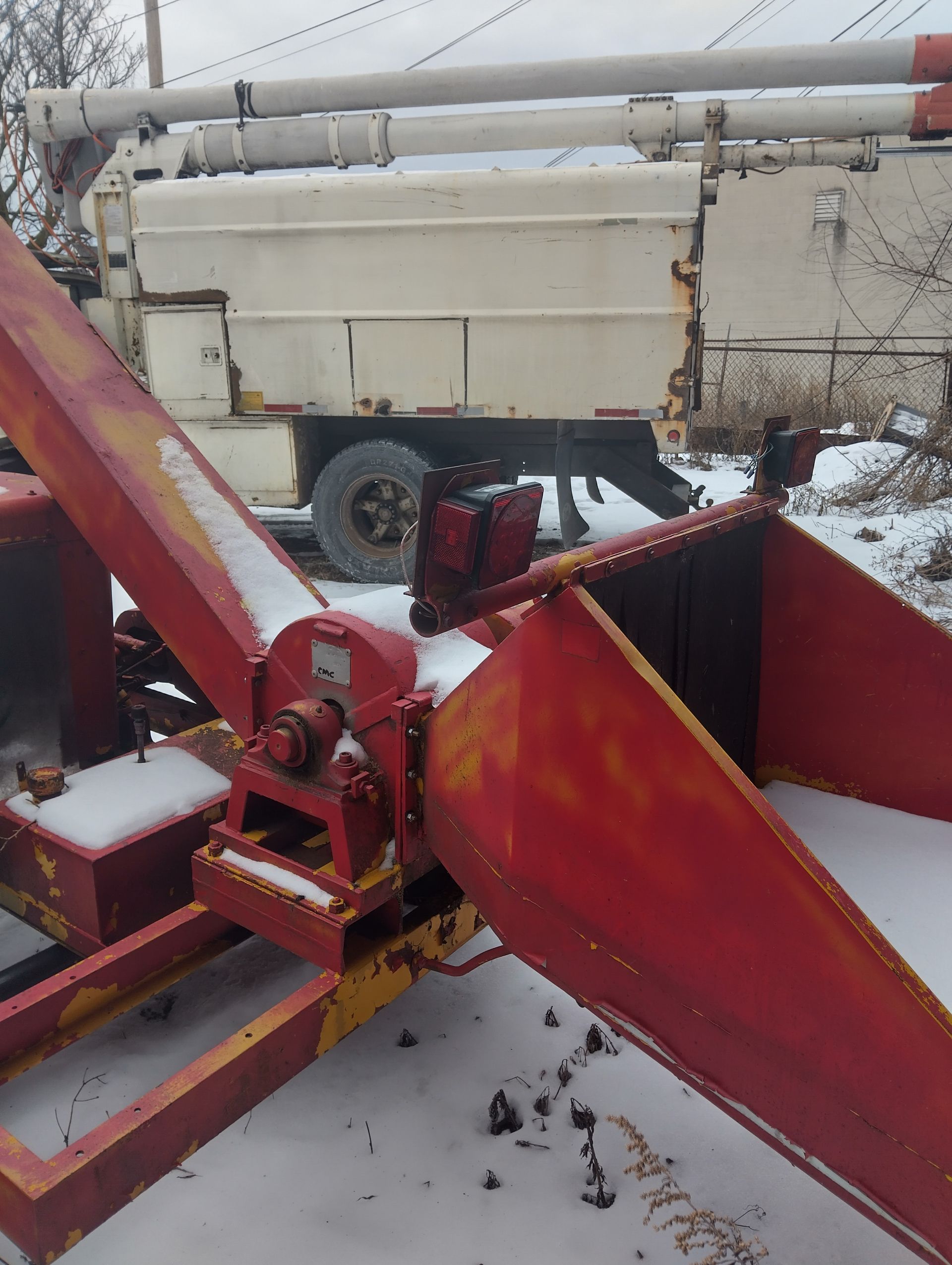 Red and yellow wood chipper, in snowy outdoor setting, with a white truck in background.