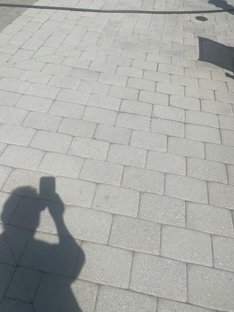 Shadow of person taking photo with phone on gray brick pavement.